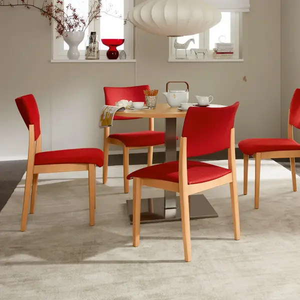 Fena – Stuhl ohne Griffbügel mit Polsterung, ideal für Gemeinschaftsbereiche in Pflegeeinrichtungen Fena-Stuhlserie ohne Griffbügel mit gepolsterter Sitzfläche und Rückenlehne – vier Stühle um einen Tisch in wohnlichem Aufenthaltsraum