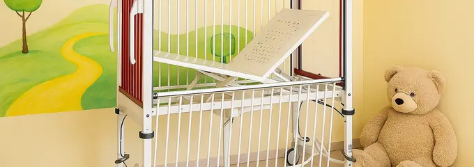 Project sketch of the planned new children's bed from Stiegelmeyer In a sketch generated with AI, the children's bed with red head and footboards stands in front of a yellow wall with a painted landscape motif. A large teddy bear sits on the floor next to the bed.